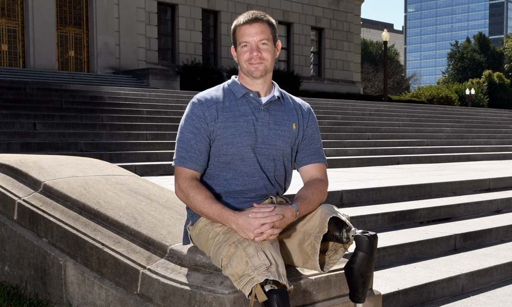Josh Bleill sits smiling on the steps with his hands crossed