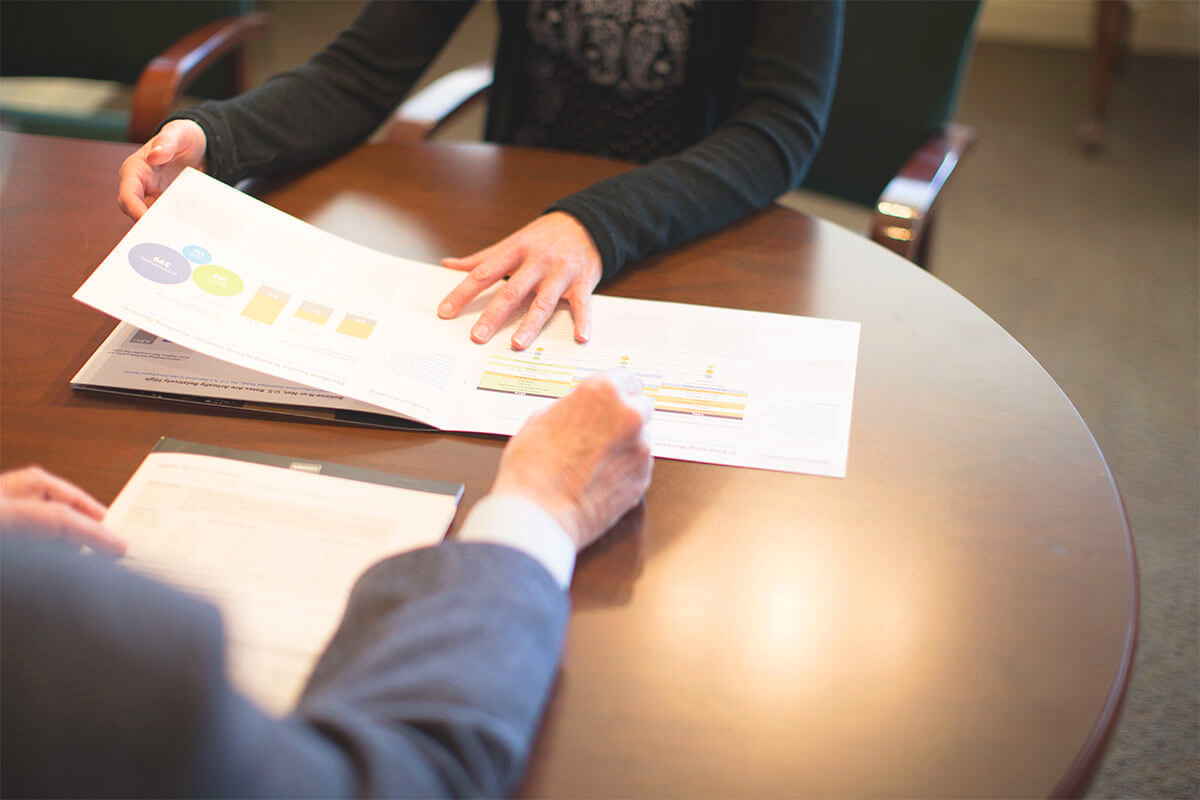 An insurance broker sits across the table from a client helping her to understand the charts and diagrams.