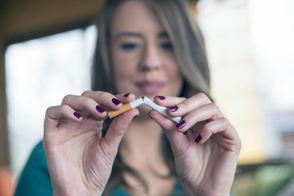 A young woman is breaking a cigarette in half symbolizing a break in the smoking addiction cycle.