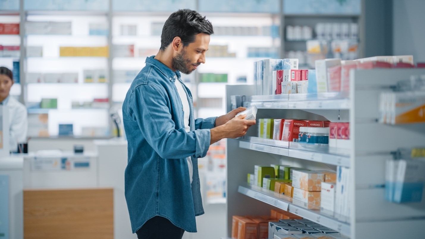 Man standing in pharmacy deciding between two products to purchase from 