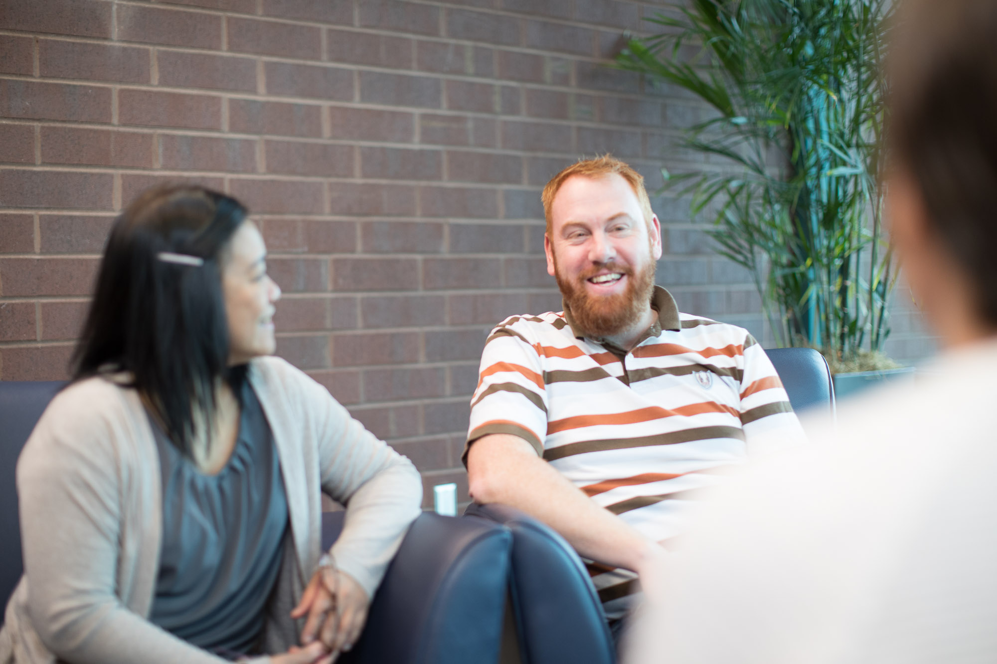 A man and woman are sitting together smiling while talking to someone across the room.